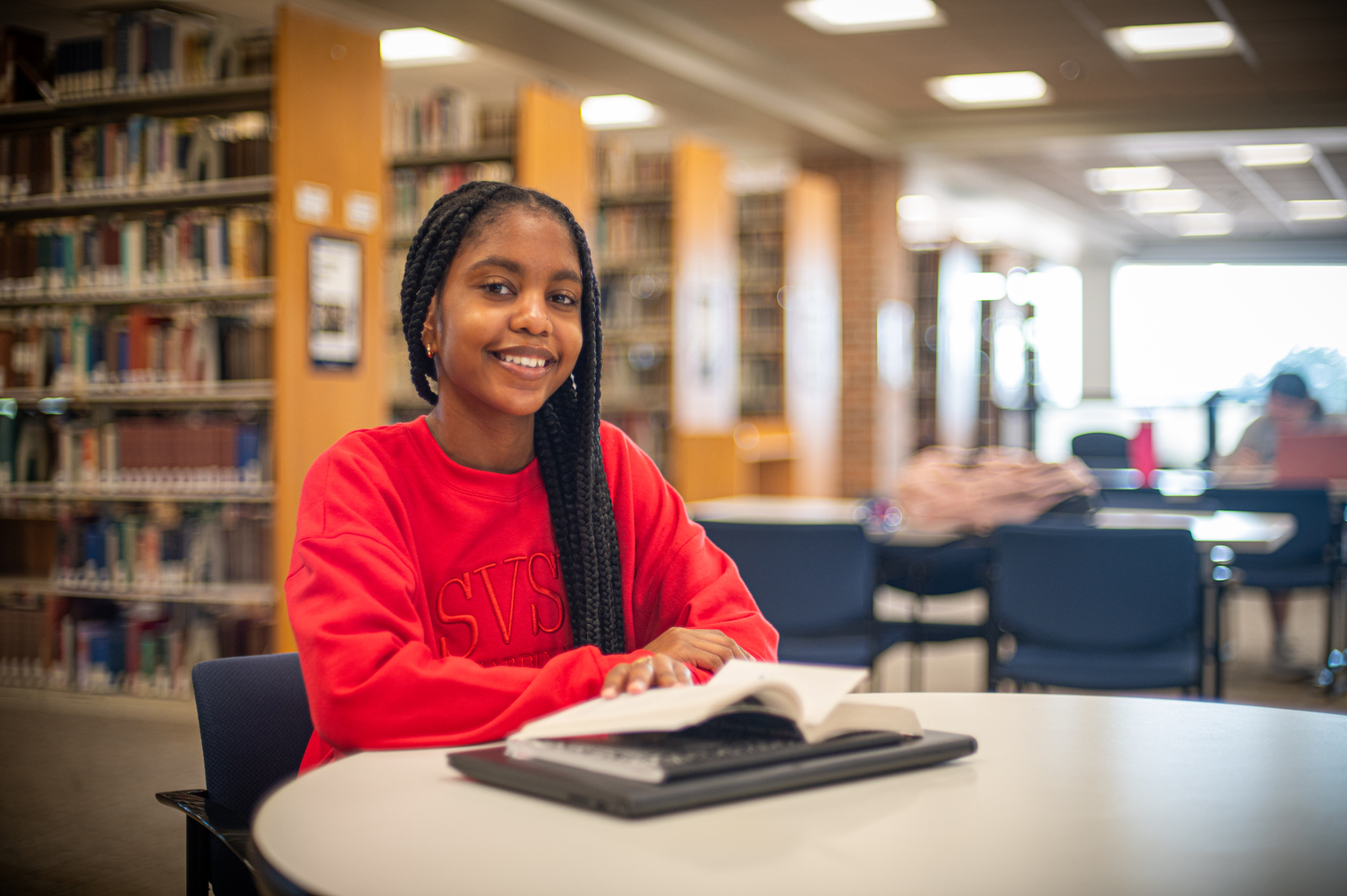 Student in red sweatshirt at library table with book